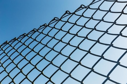 View of the blue sky through a chain link fence.